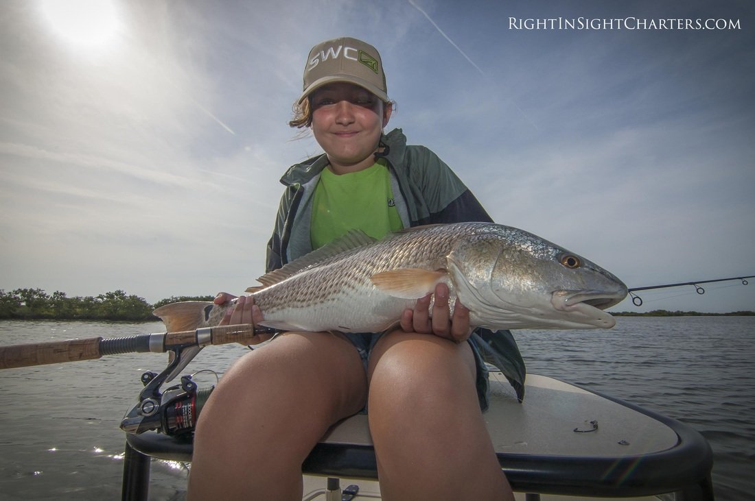 A little girl is seating on the casting platform of the East Cape Glide while holding a redfish in the Indian lagoon.