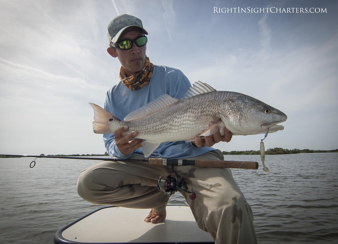 Capt. Justin Price holding a redfish from the Indian River lagoon standing on the casting platform of East Cape skiff.